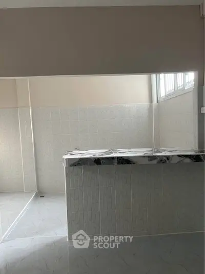 Modern kitchen with marble countertop and tiled walls, featuring ample natural light.