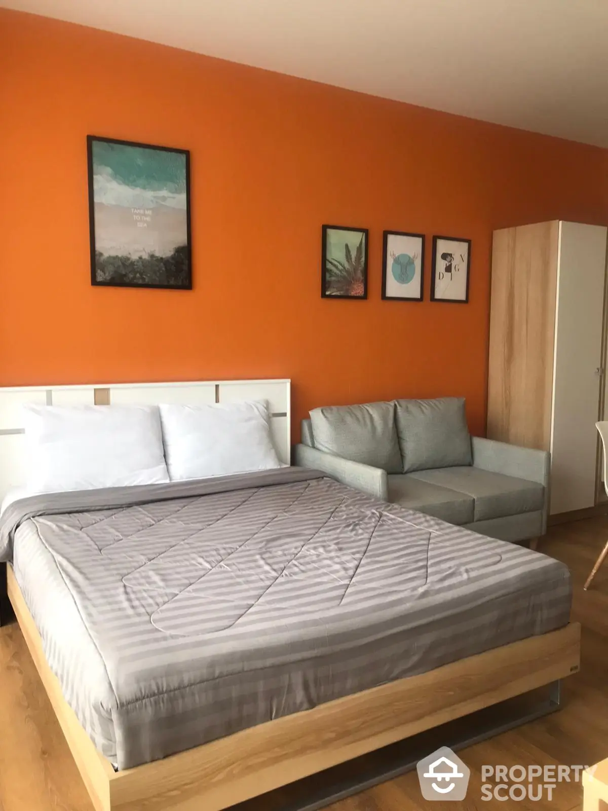 Spacious bedroom with a vibrant orange accent wall, modern furnishings, and a cozy sitting area, ideal for relaxation and comfort.