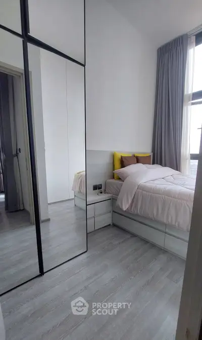 Modern bedroom with mirrored wardrobe and large window for natural light.