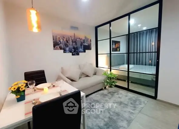 Modern living room with cozy dining area and glass partition to bedroom, featuring stylish decor.