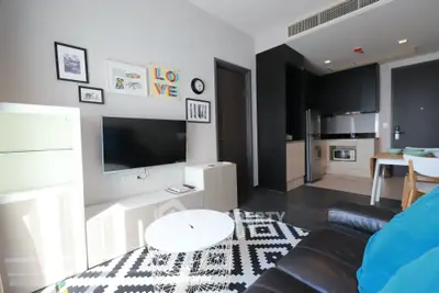 Modern living room with stylish decor and open kitchen layout, featuring a cozy seating area and wall-mounted TV.