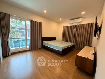 Spacious bedroom with large window and modern furnishings in a well-lit apartment.