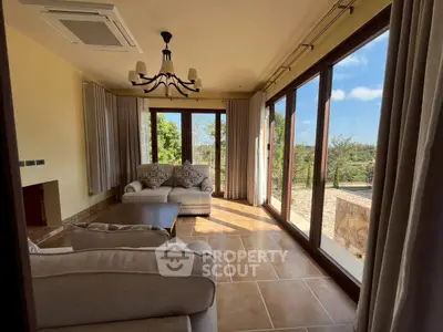 Spacious living room with large windows and scenic garden view, featuring elegant furniture and natural light.