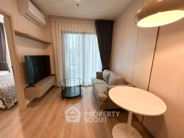 Modern living room with cozy sofa, round table, and large TV, featuring floor-to-ceiling window.
