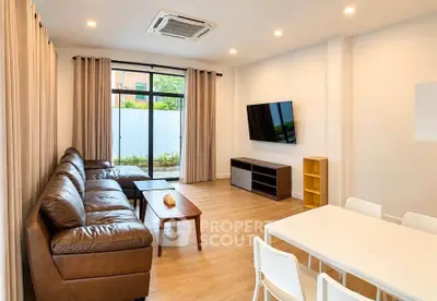 Spacious modern living room with leather sofa, wall-mounted TV, and dining area in a bright, airy setting.