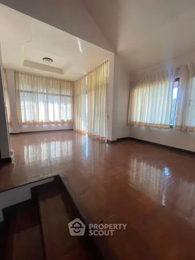 Spacious sunlit room with wooden flooring and large windows, perfect for a cozy living area.