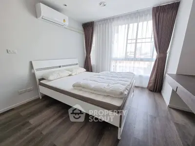 Modern bedroom with large window, wooden flooring, and air conditioning in a stylish apartment.