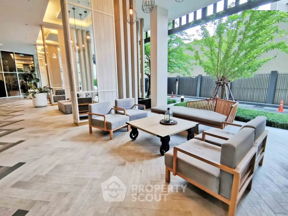 Elegant outdoor seating area with modern furniture and lush greenery in a stylish building entrance.