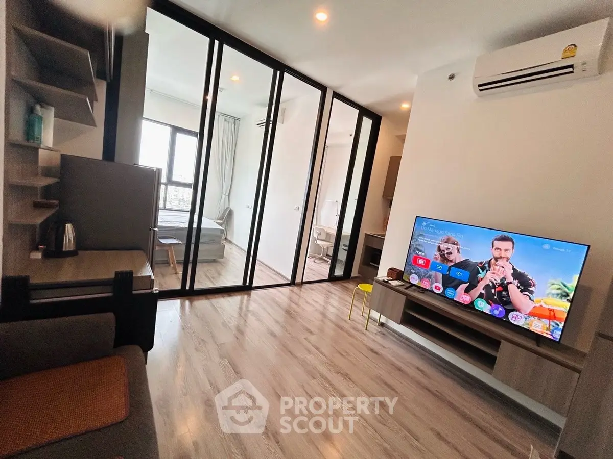 Modern living room with large TV and glass partition leading to bedroom