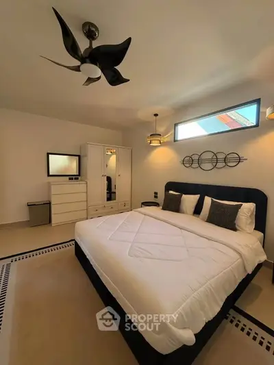 Modern bedroom with stylish decor, featuring a large bed, sleek ceiling fan, and ample natural light.