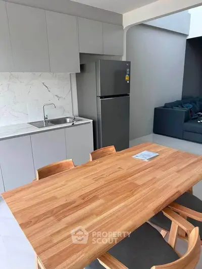 Modern kitchen with sleek cabinetry and dining area featuring wooden table and chairs.