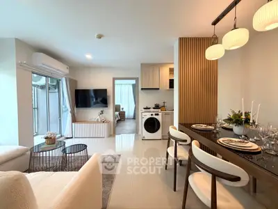 Modern open-plan living room with dining area and washing machine, featuring elegant decor and ample natural light.