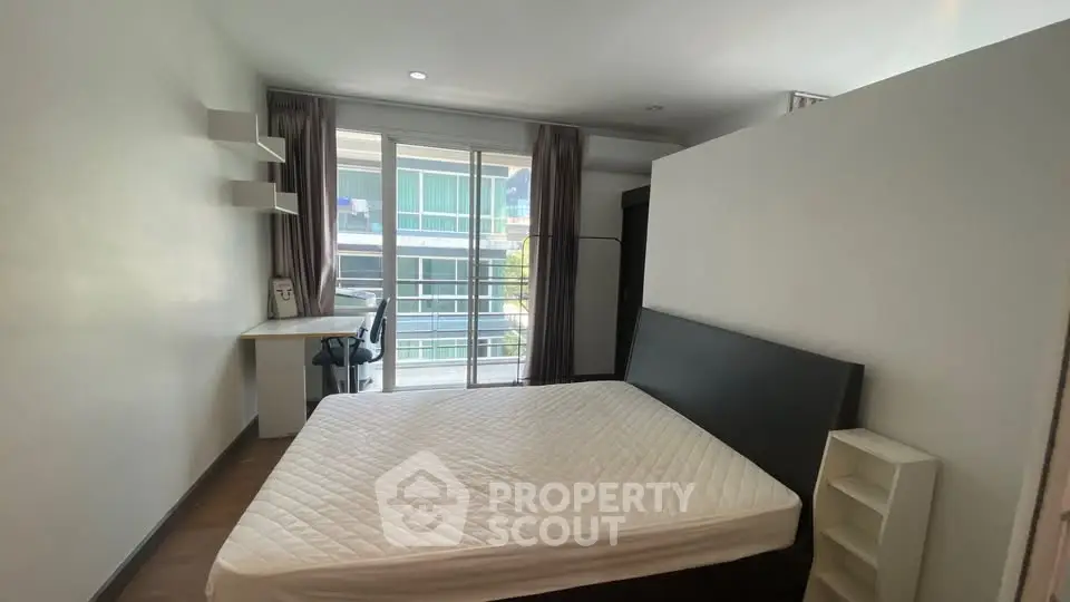 Modern bedroom with balcony access and study area in a bright apartment.