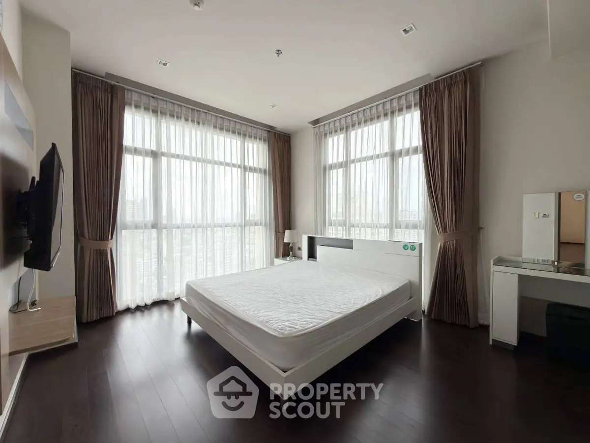 Spacious bedroom with large windows and modern furnishings in a high-rise apartment.