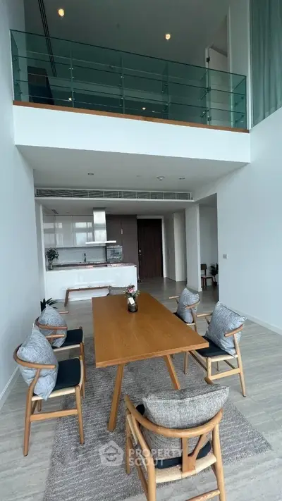 Spacious double-height living room with modern open kitchen, elegant dining set, and a cozy upper-level loft area with glass balustrade, offering a luxurious and airy ambiance.