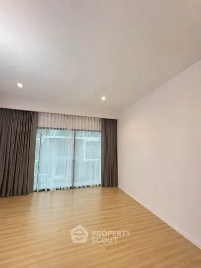 Spacious empty room with wooden flooring and large window, perfect for customization.