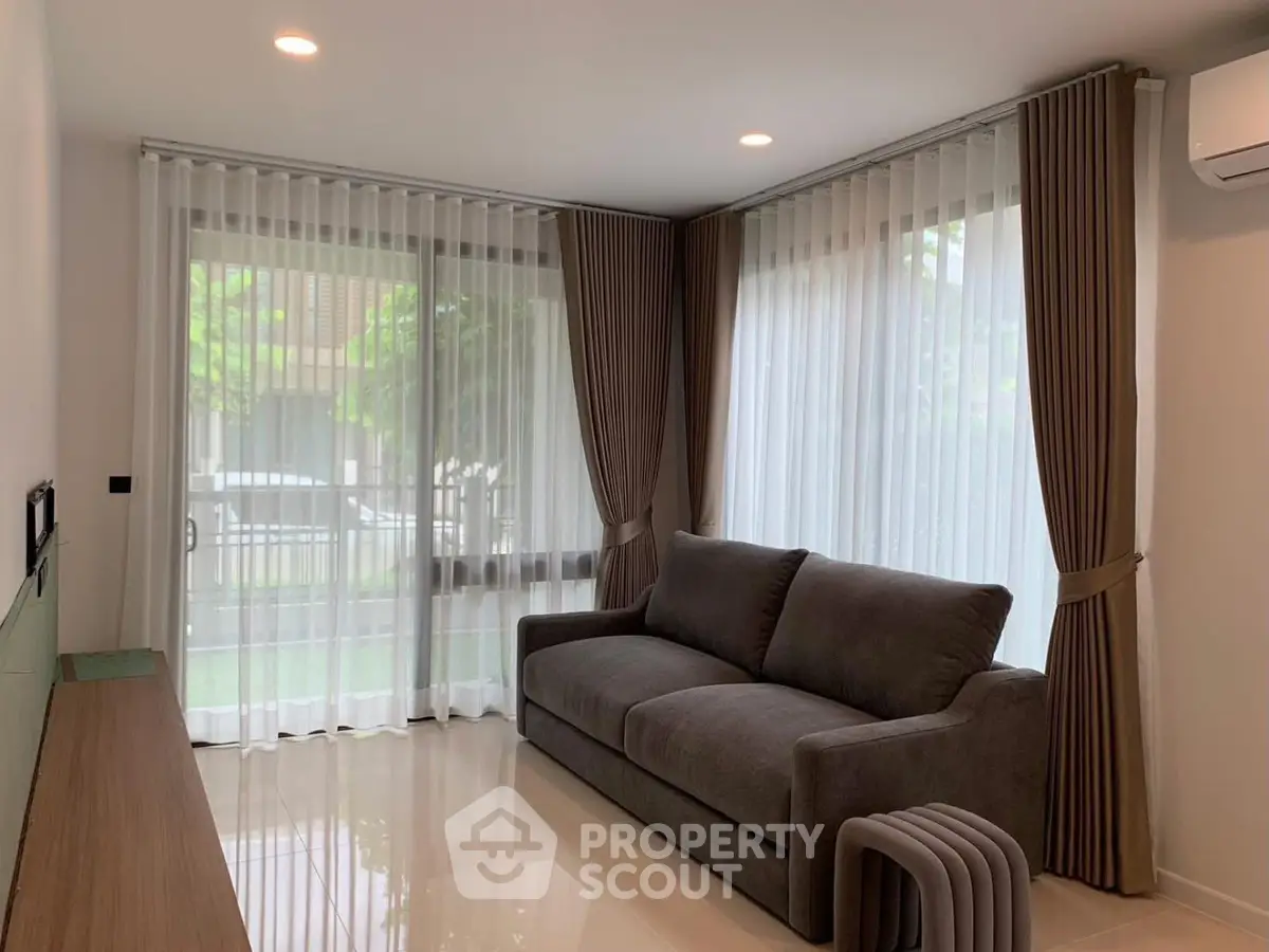 Modern living room with large windows and elegant curtains, featuring a comfortable sofa and stylish decor.