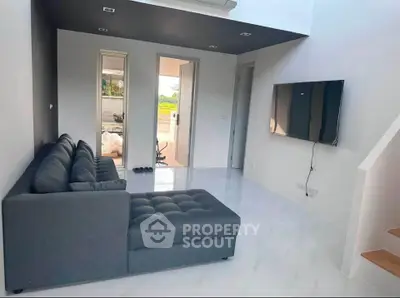 Modern living room with sleek gray sofa and wall-mounted TV, featuring minimalist design and bright natural light.