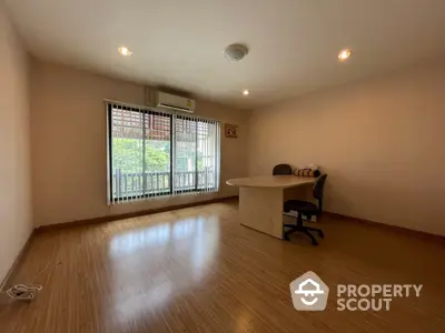 Spacious and well-lit study room with glossy hardwood floors and a large window with protective grills, ideal for a home office setup.