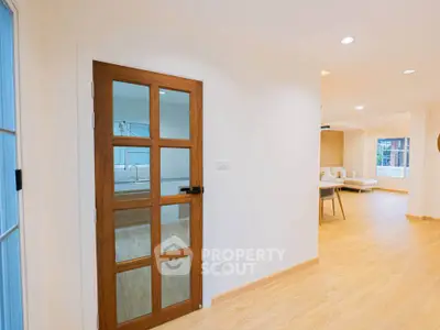 Spacious modern living room with wooden flooring and glass door, featuring open layout and natural light.