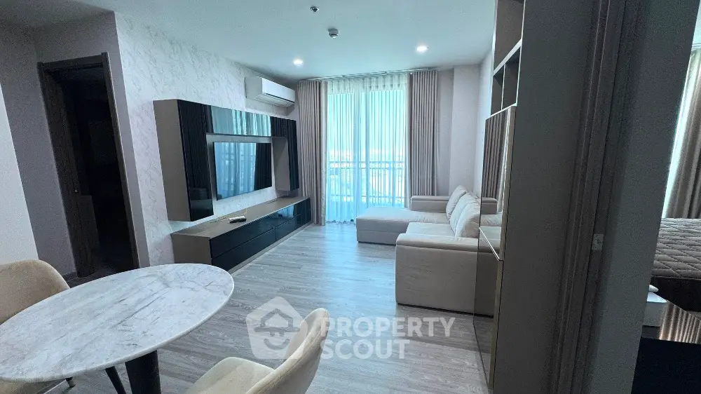 Modern living room with sleek furniture and large TV, featuring a cozy dining area and ample natural light.