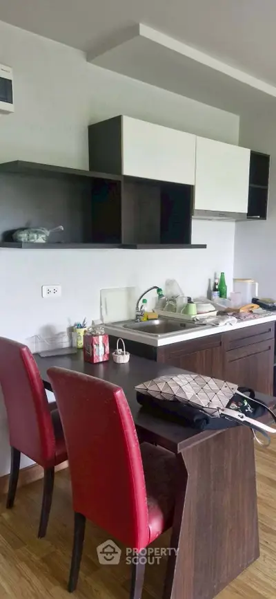 Modern kitchen with sleek cabinets and dining area featuring red chairs.