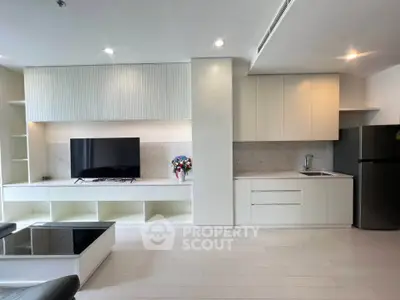 Modern living room with sleek white cabinetry and integrated kitchen area, featuring a large flat-screen TV and stylish decor.