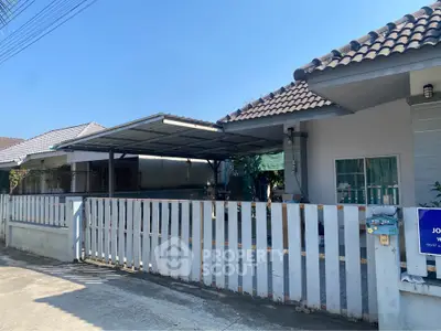 Charming single-story home with gated driveway and tiled roof under clear blue sky.