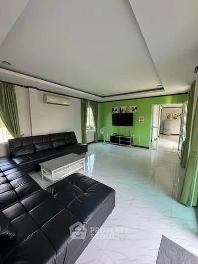 Spacious modern living room with sleek black sofas and green accents, perfect for relaxation and entertainment.