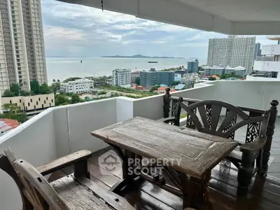 Stunning balcony view with wooden furniture overlooking the ocean and city skyline.