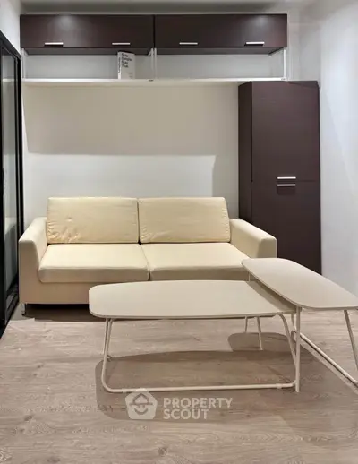 Modern living room with beige sofa and sleek coffee tables on wooden flooring.
