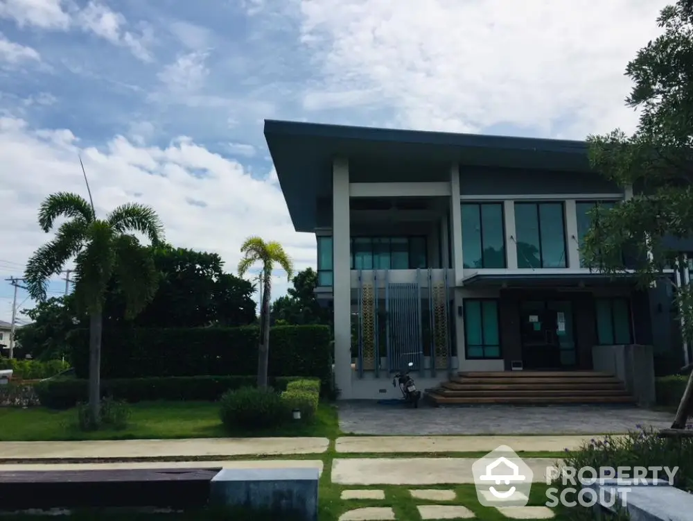 Modern two-story home with expansive glass facade, surrounded by lush greenery and a well-manicured lawn, showcasing contemporary architecture and luxury living.