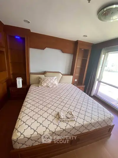 Spacious bedroom with elegant wooden built-in shelves and large window for natural light.