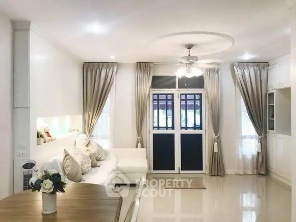 Elegant living room with modern decor and large windows, featuring a cozy white sofa and stylish curtains.