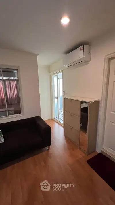 Cozy living room with wooden flooring and air conditioning, featuring a modern sofa and mirrored cabinet.