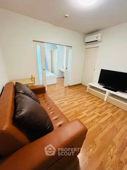 Modern living room with brown leather sofa and flat-screen TV, featuring wooden flooring and sliding doors.