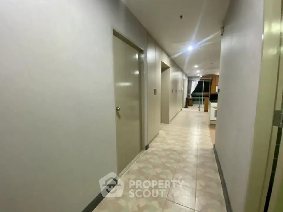 Spacious corridor in modern apartment building with tiled flooring and neutral walls.