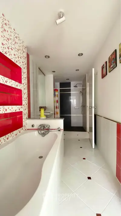 Spacious bathroom with modern design and bathtub, featuring stylish red accents and sleek tiles.
