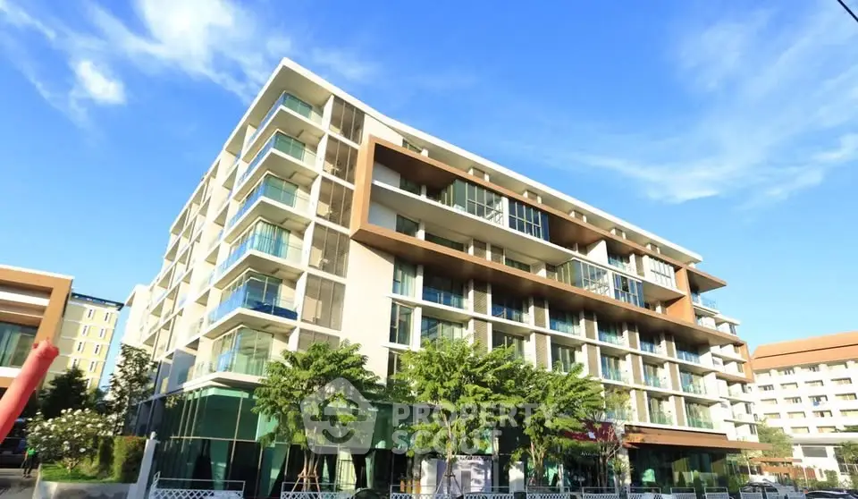 Modern multi-story residential building with glass balconies and lush greenery.