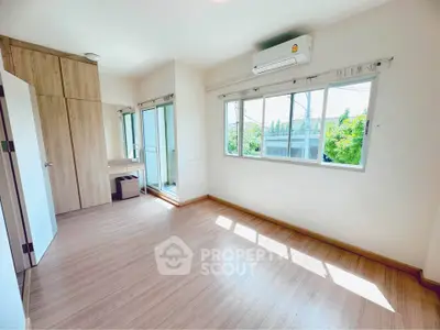 Spacious bedroom with large windows and wooden flooring, featuring built-in wardrobe and air conditioning.