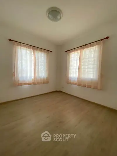 Bright empty room with wooden flooring and sheer curtains, perfect for customization.