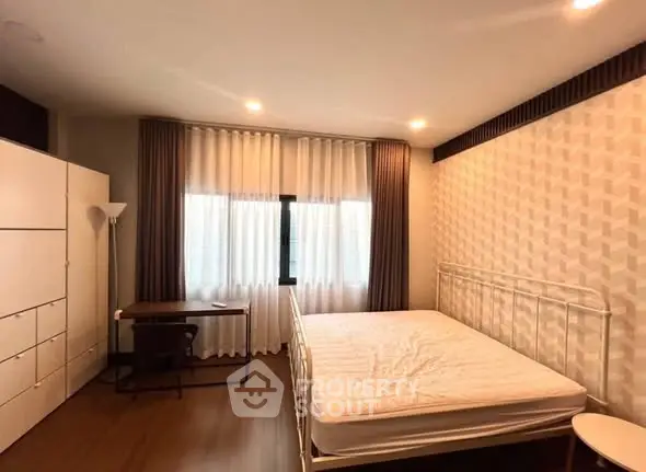 Spacious bedroom with modern decor, featuring a large window and stylish furniture.