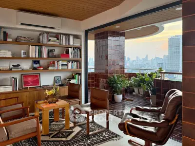 Spacious living room with city view and balcony, featuring modern furniture and built-in bookshelves.