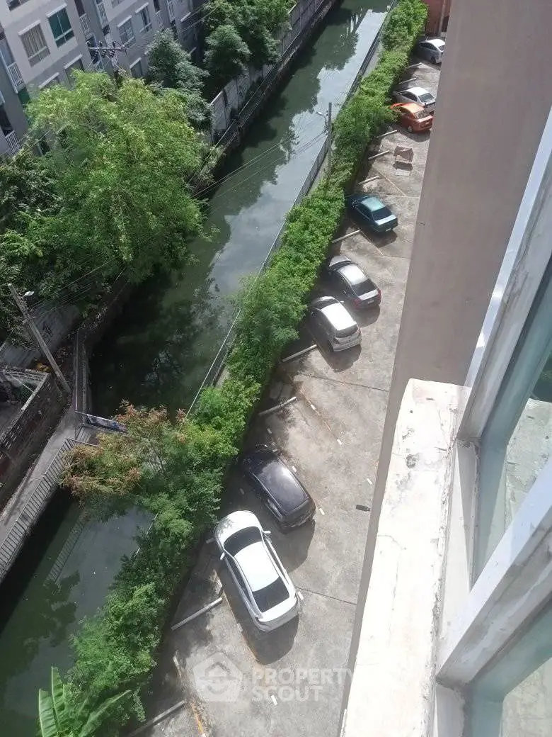 Aerial view of parking area beside a canal with parked cars and lush greenery.