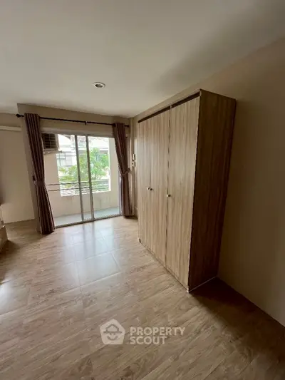 Spacious bedroom with wooden flooring and large window offering natural light and garden view.