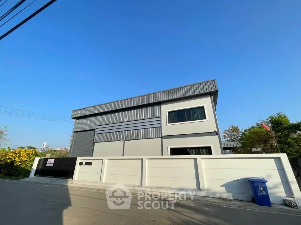 Modern industrial-style building with sleek facade and gated entrance in sunny setting.