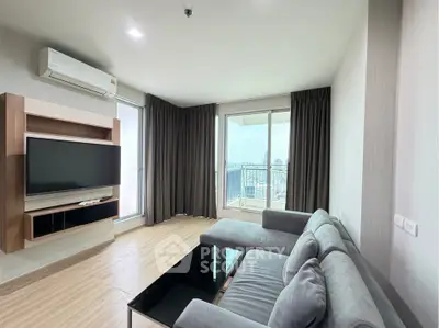 Modern living room with large windows and city view, featuring a sleek sofa and wall-mounted TV.