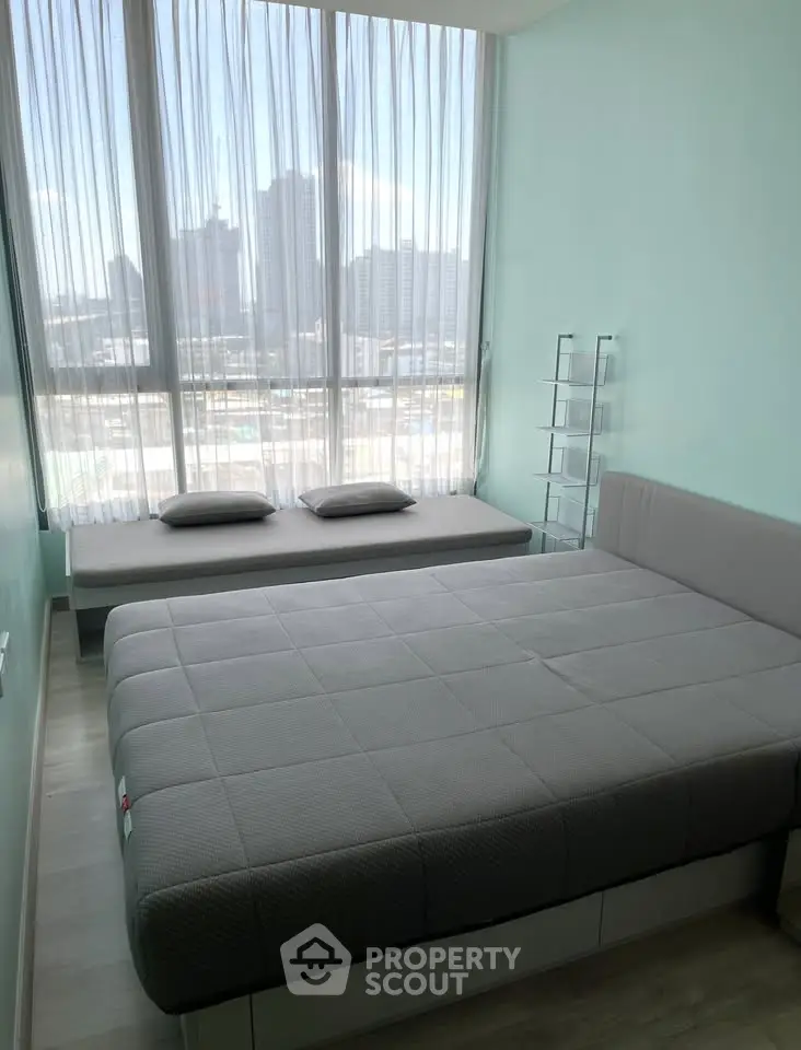 Modern bedroom with large windows and city view, featuring stylish gray bedding and minimalist decor.