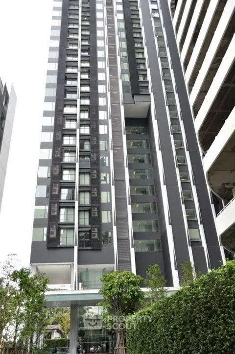 Modern high-rise building with sleek design and lush greenery at the entrance.