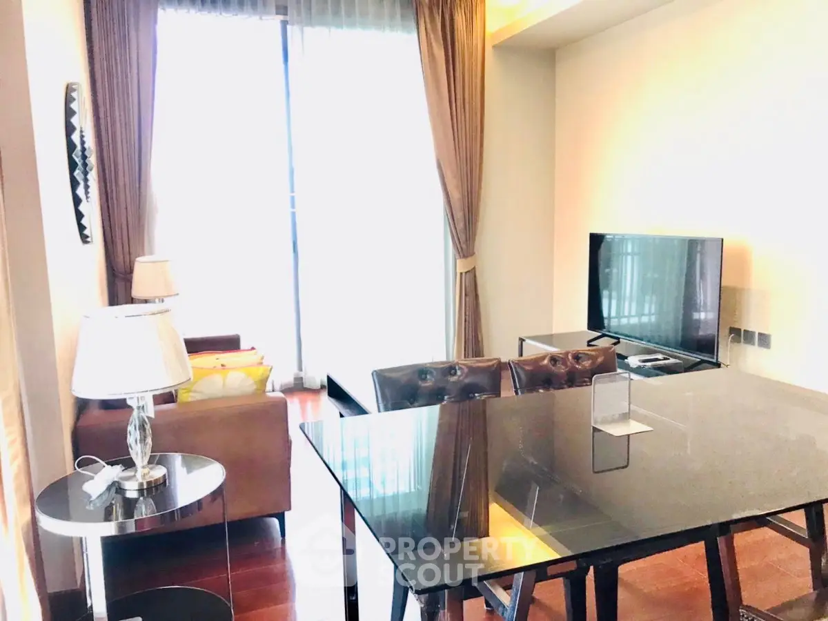 Modern living room with elegant decor and natural light, featuring a sleek glass dining table and cozy seating area.